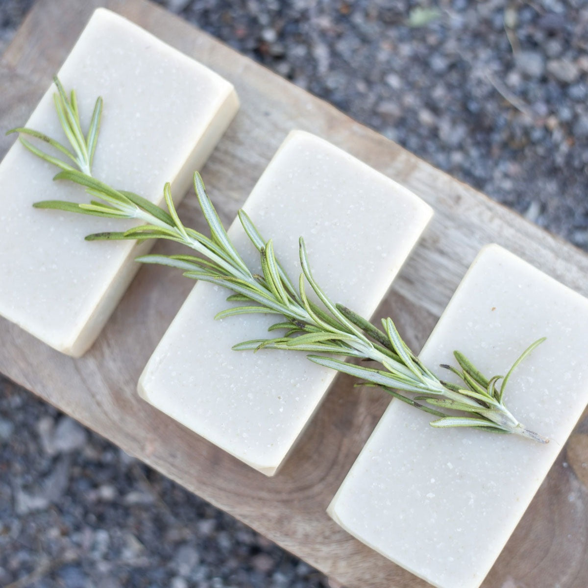 3 all natural bar soaps that are lined up, topped with rosemary herbs and layer down